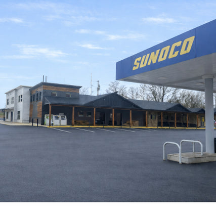Convenience StoreA Sunoco gas station with a blue canopy and yellow logo is in front of a rustic two-story building with wood accents under a cloudy sky, evoking a quiet, rural atmosphere.