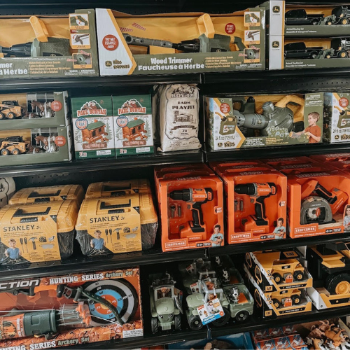 Toy store shelf filled with toy tools and vehicles, featuring lawn equipment, drills, and trucks. Bright packaging creates an inviting and playful atmosphere.