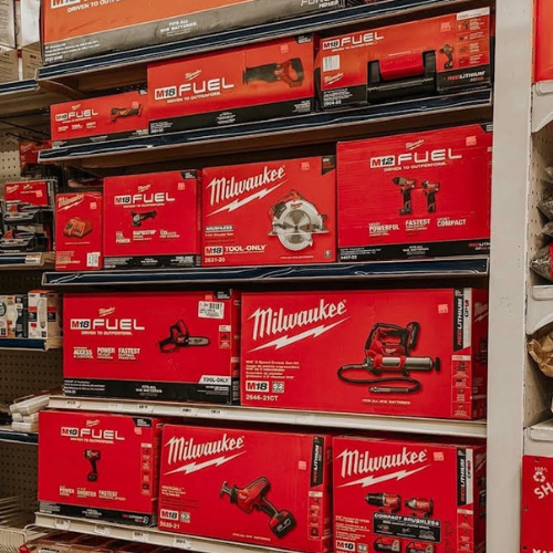 Shelves of red Milwaukee power tool boxes in a store aisle. Varied tools, including a saw and drill, neatly arranged, conveying a professional feel.